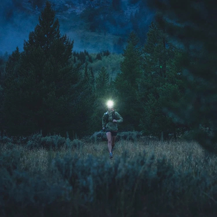 Runner with a headlamp crossing a meadow at dusk